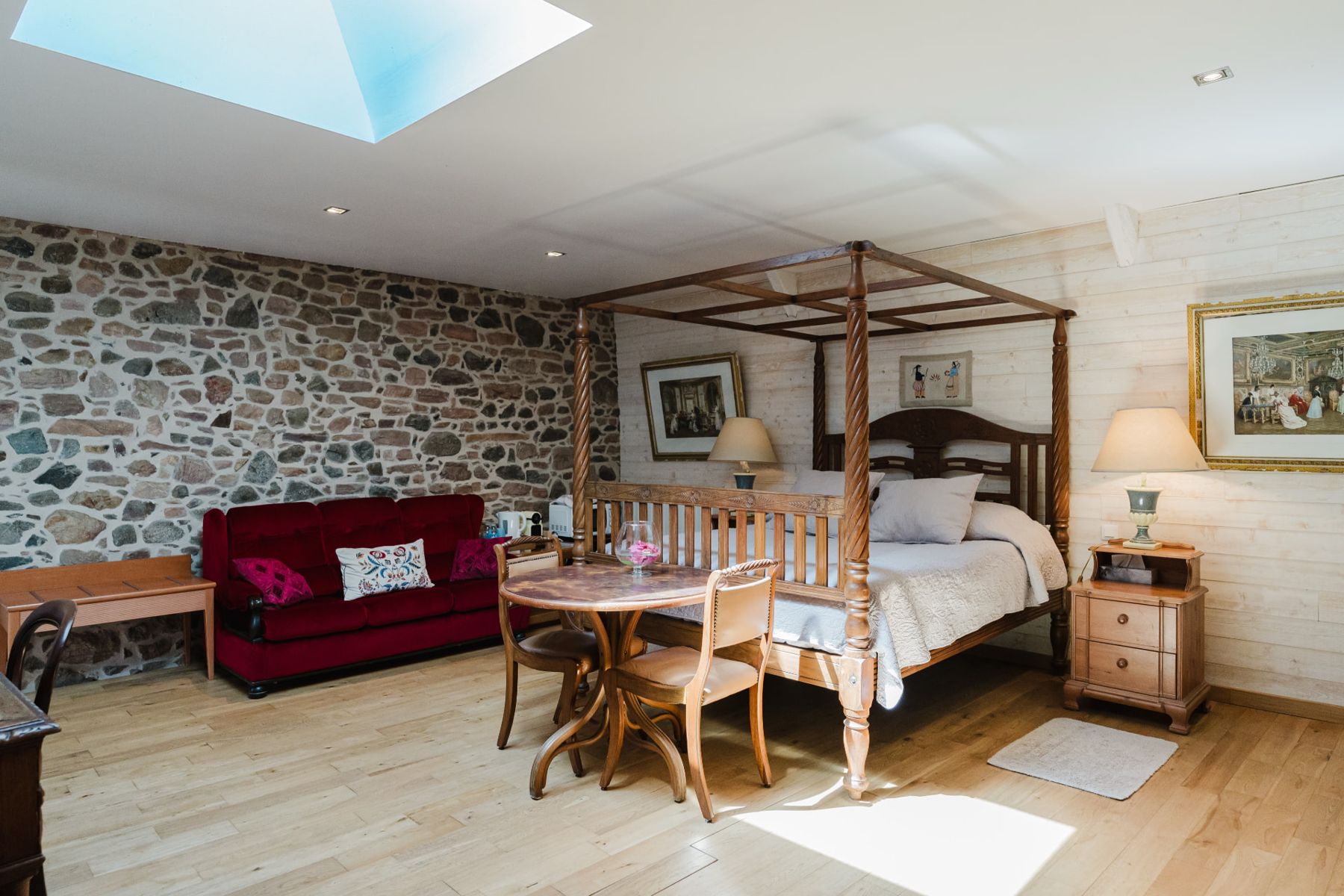 Coin salon avec canapé rouge et mur de pierre apparente dans la Chambre Double Confort