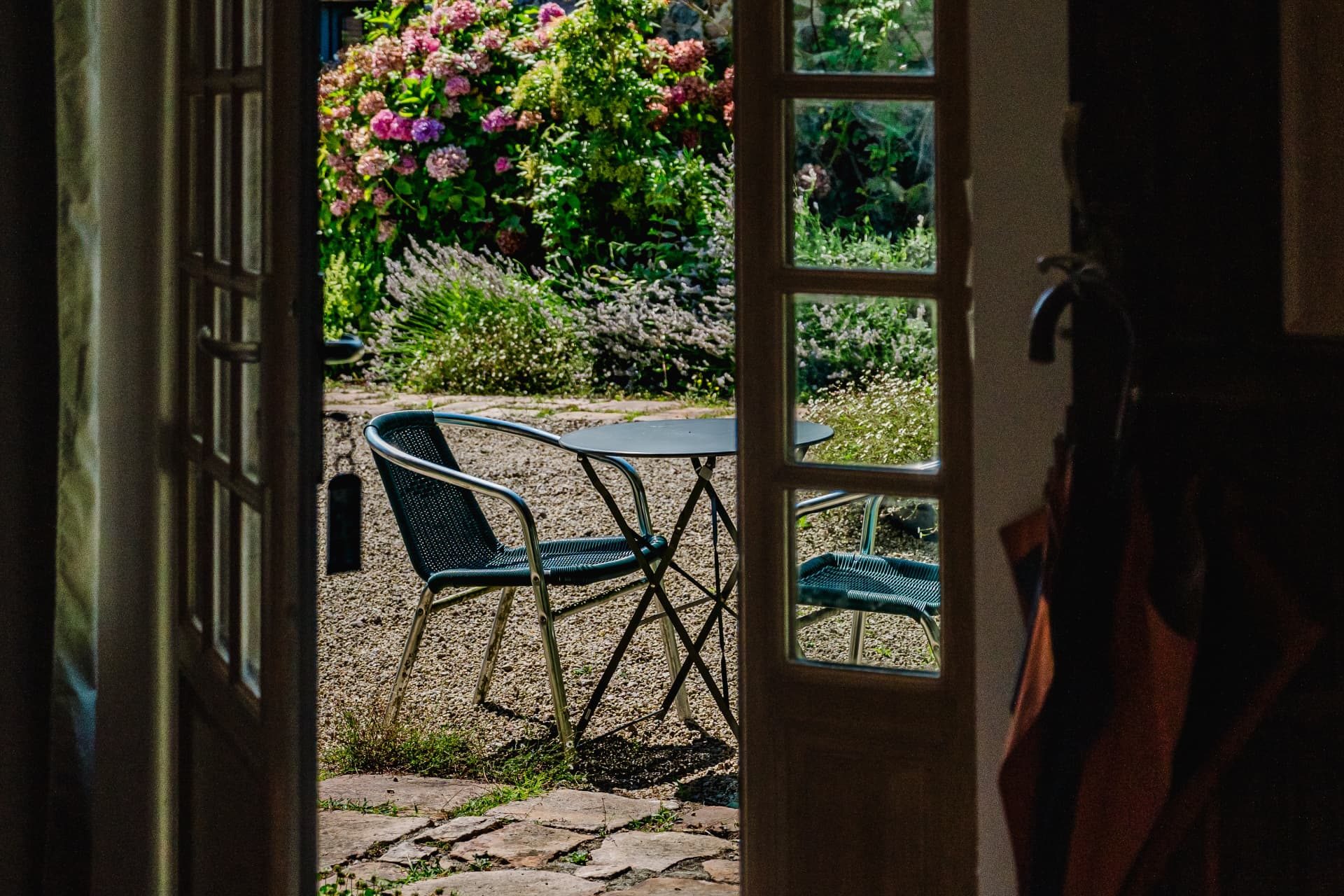 Porte-fenêtre ouverte sur la cour fleurie et le salon de jardin